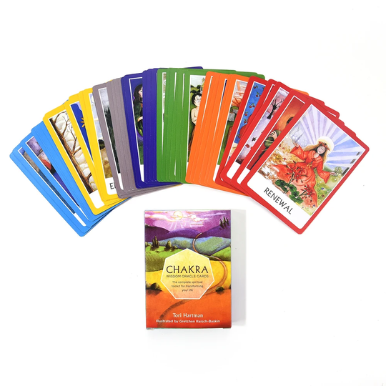 A spread of chakra oracle cards arranged by the seven chakra colours, from root red up to crown violet, on a linen cloth