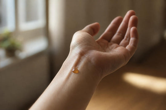 A drop of attār oil applied to the inner wrist, catching warm window light, testing fragrance on skin rather than paper