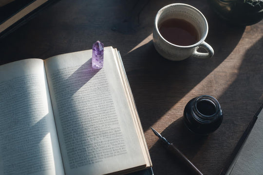 Amethyst crystal point resting on an open book on a wooden writing desk with morning raking light