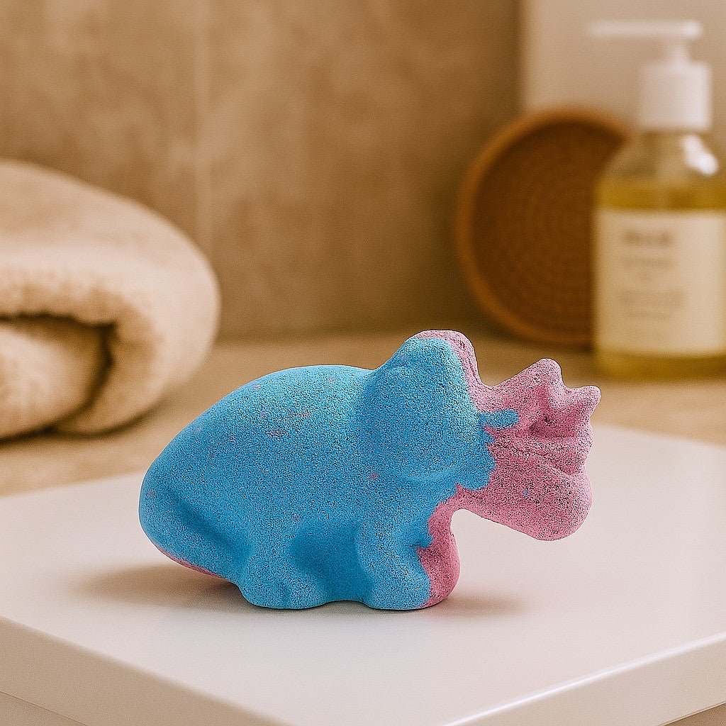 Blue and pink bath bomb shaped like a dinosaur on a white surface with a blurred background.