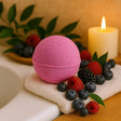 Pink bath bomb on a towel with berries and a candle in the background