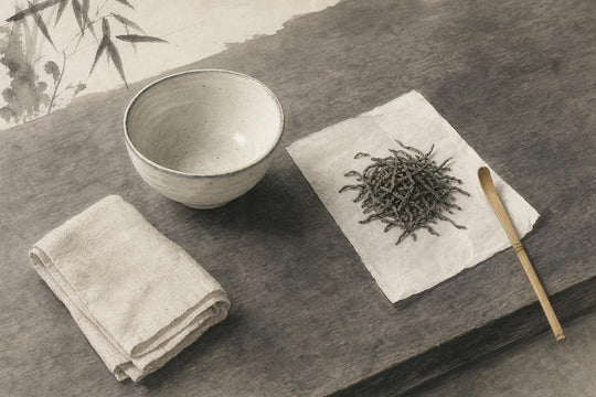Een schrijftafel met een keramische kom, losse theeblaadjes en een bamboeschepje, de minimale benodigdheden voor een theeritueel.