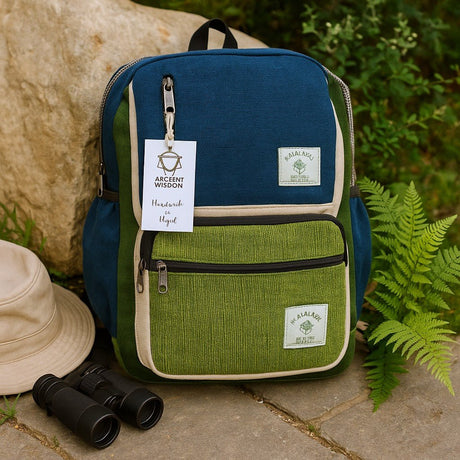Two-tone blue and green backpack with binoculars and a hat on a stone surface with plants in the background