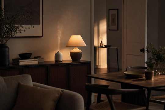 An open-plan living space with an electric diffuser releasing mist, and a reed diffuser visible in the hallway beyond
