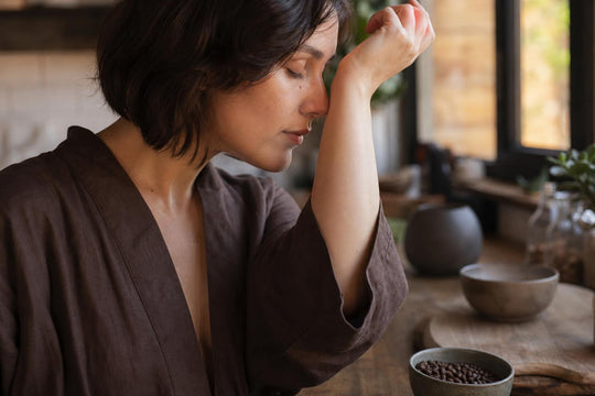 A hand raised to the nose beside a small bowl of coffee beans on a kitchen counter