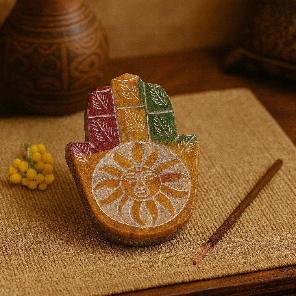 Decorative wooden hand with sun design on a textured surface with incense and flowers.