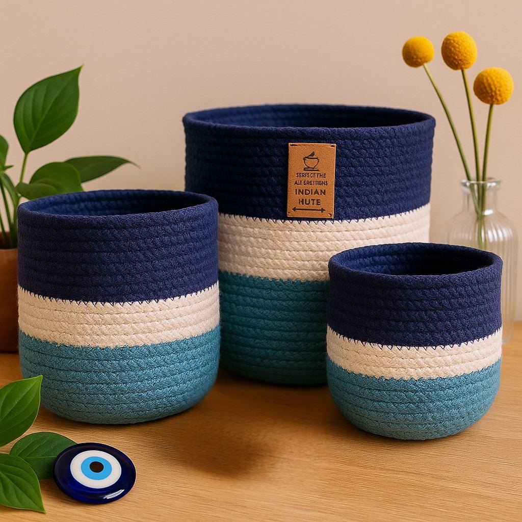 Set of three blue and white woven baskets on a wooden surface with a plant and vase in the background.