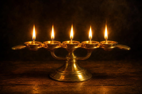 Uma lamparina de aarti de latão, com cinco pavios acesos e cinco chamas constantes contra um fundo escuro.