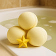 Three yellow bath bombs with a star-shaped object on a bathtub rim