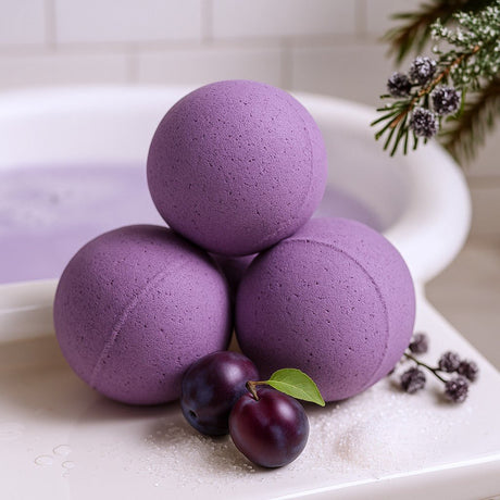 Three purple bath bombs on a white surface with plums and a plant.