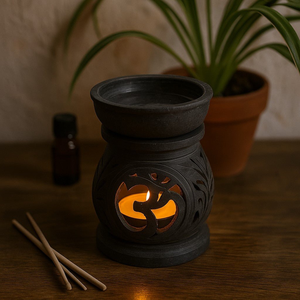 Black ceramic oil burner with a lit candle inside on a wooden surface, surrounded by a plant and essential oils.