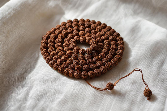 En hoprullad rudraksha-mala med 108 pärlor på ljust linne i mjukt morgonljus.