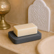 Bar of soap on a black soap dish with decorative elements in the background