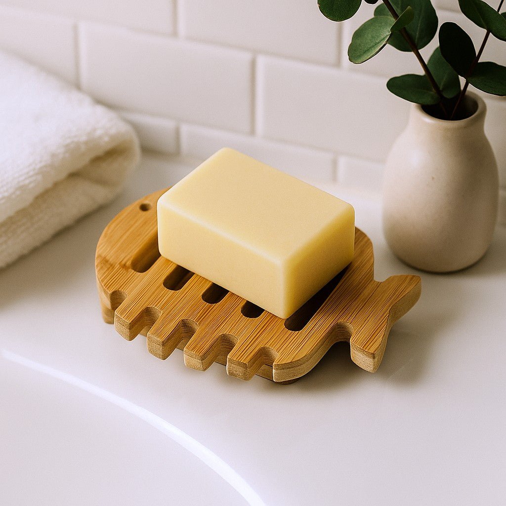 Bar of soap on a wooden soap dish with a plant and towel in the background