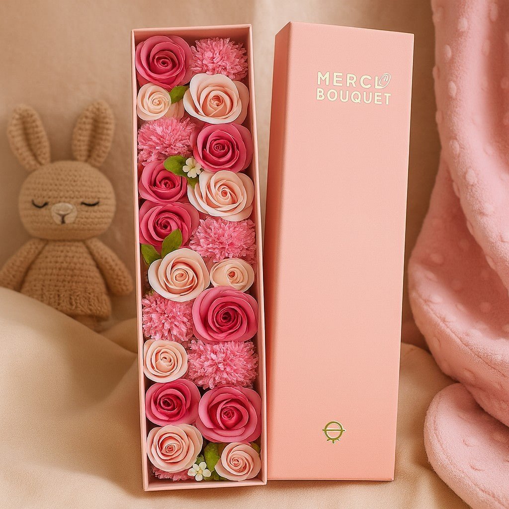 Pink floral arrangement in a box with 'MERCi Bouquet' branding, next to a plush toy on a soft surface.