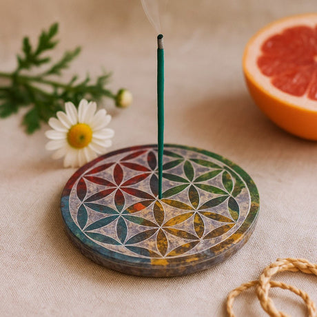 Incense burner with a smoking incense stick on a decorative mat, next to a daisy and half a grapefruit.