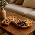 Wooden snack tray with various nuts and dried fruits on a wooden table.