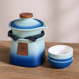 Ceramic teapot with gradient blue design and wooden lid, accompanied by matching bowls on a wooden surface.