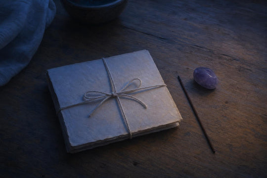 Une lettre pliée et non envoyée, attachée avec une ficelle de coton, à côté d'un bâton d'encens éteint et d'une petite pierre d'améthyste sur du bois.