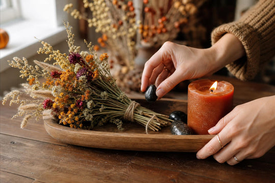 Hands arranging dried flowers and a rust candle on an autumn altar