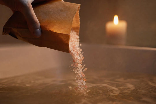 Himalayabadsalt hälls i ett levande ljus-belyst bad, där kornen fångar det varma ljuset medan de löses upp.
