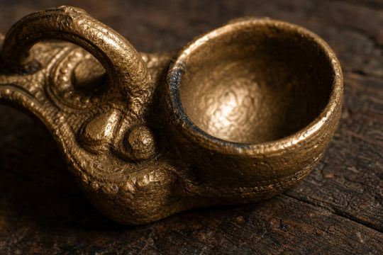 Close-up of the textured surface of a Dhokra brass diya showing the hand-cast relief detail and casting marks