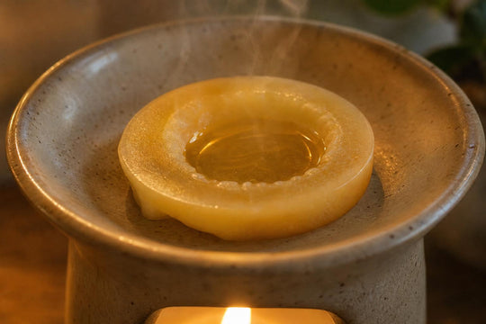 Detailní pohled na napůl roztavený disk vonného vosku v keramické misce aromalampy, kterou zespodu prozařuje teplé světlo