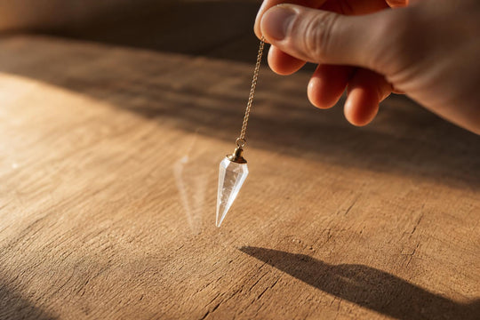 Una mano sostiene un péndulo de cristal por su cadena mientras la piedra oscila formando un arco