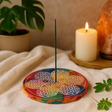 Colorful circular incense holder with a lit candle and plant in the background