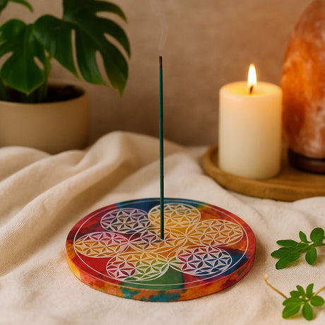 Colorful circular incense holder with a lit candle and plant in the background