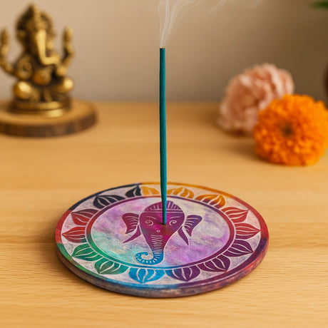 Incense stick on a colorful circular holder with a statue and flowers in the background
