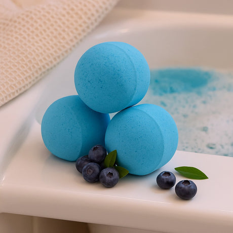 Three blue bath bombs with blueberries on a bathtub rim
