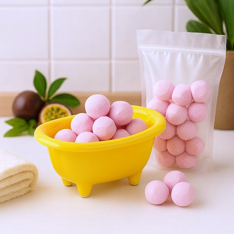 Pink bath bombs in a yellow bathtub-shaped container with a bag of more bath bombs on a white surface.