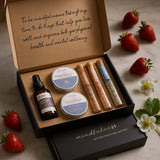 Gift set with mindfulness theme, including a bottle and containers, on a marble surface with strawberries and flowers.