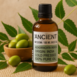 Bottle of 'Ancient Wisdom' neem base oil with green olives and leaves on a textured surface.