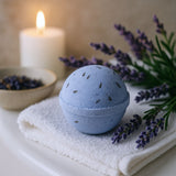 Blue bath bomb with lavender flowers and a candle on a white surface