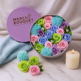 Colorful floral arrangement in a Merci Bouquet box on a marble surface with a candle.