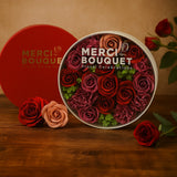Merci Bouquet floral arrangement in a round container with a red heart-shaped box in the background.