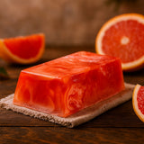 Bar of red soap with grapefruit slices on a wooden surface