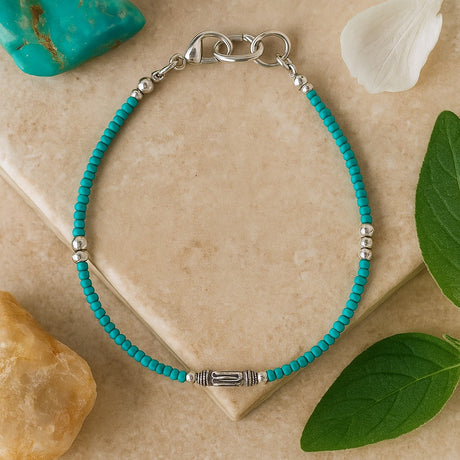 Turquoise beaded bracelet with silver clasp on a beige stone surface with green leaves and stones.