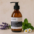 Brown bottle of massage and bath oil with a label, surrounded by lavender flowers and green leaves on a beige background.