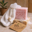 Pink bar of soap with 'Fenman Soap' branding, a white washcloth, and a wooden tag on a neutral background.