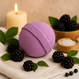 Purple bath bomb with blackberries and a candle on a neutral background
