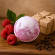 Pink bath bomb with raspberries and a gift box on a wooden surface