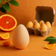 Egg on an orange background with oranges and a carton of eggs.