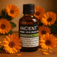 Bottle of Ancient Wisdom Calendula oil with calendula flowers on a wooden surface