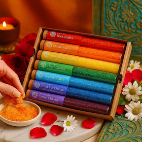 Set of colorful incense sticks labeled with chakra names on a decorative surface with flowers and candles.