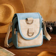 Blue and beige crossbody bag on a wooden surface with a camera and hat in the background