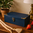 Blue wooden box with gold accents on a wooden surface with a plant and lamp in the background