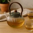 Glass teapot with wooden handle on a wooden table with two cups of tea.